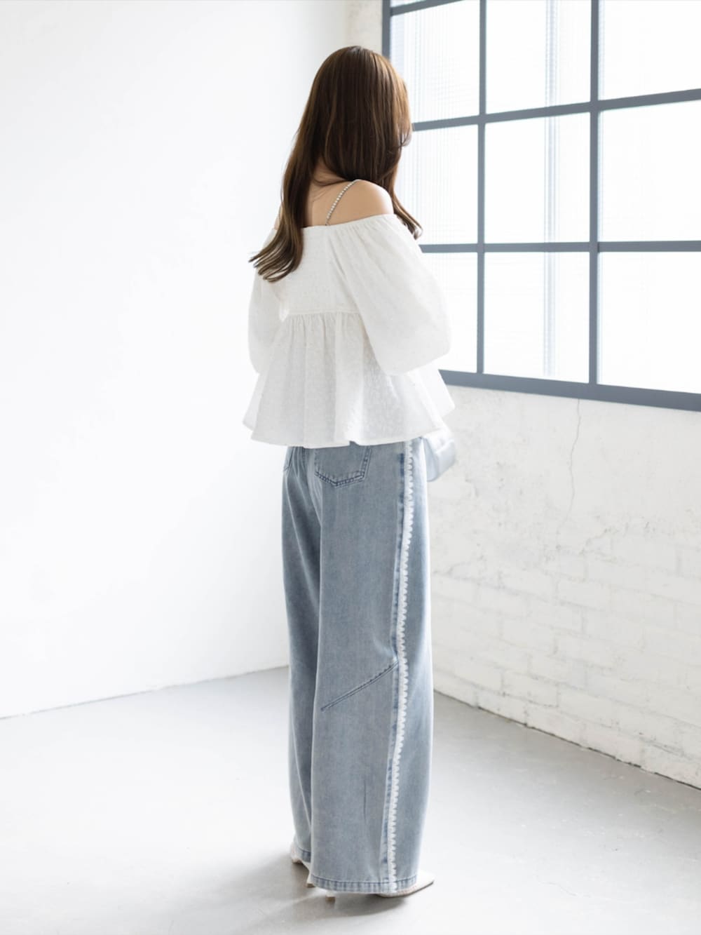 シルバー系のハンドバッグ、ブルー系のデニムパンツ、ホワイト系のパンプスを着用したレディースの春コーディネートの3枚目の写真