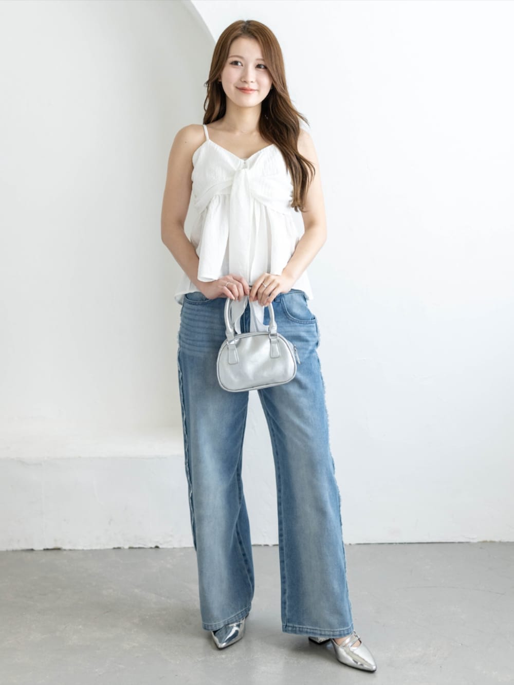 シルバー系のパンプス、ブルー系のデニムパンツ、ホワイト系のキャミソールを着用したレディースの夏コーディネートの2枚目の写真