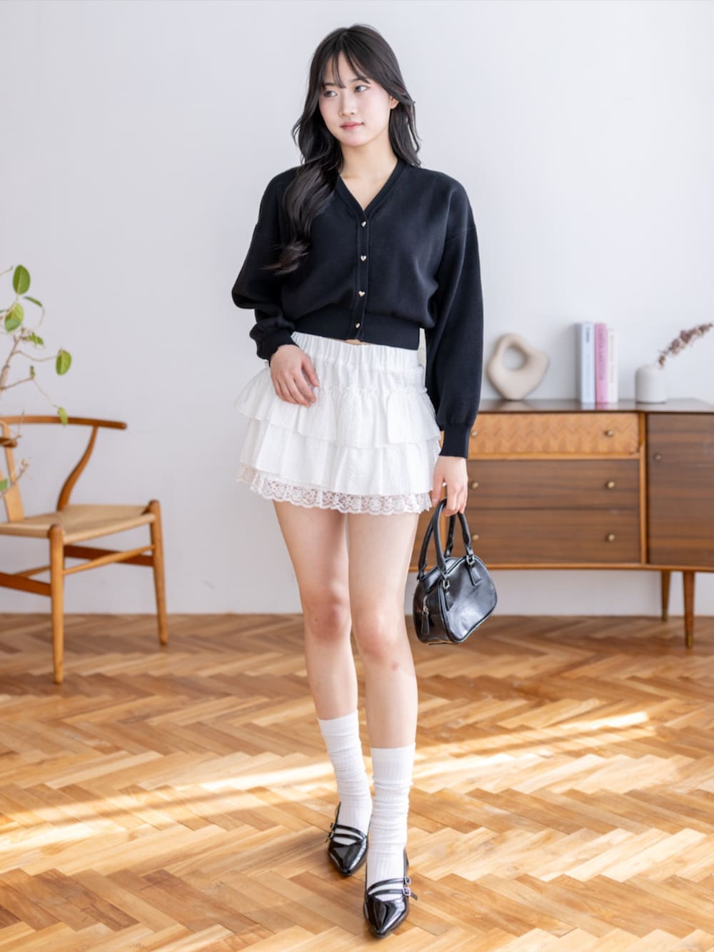 ブラック系のパンプス、ホワイト系のスカート、ブラック系のカーディガン/ボレロを着用したレディースの夏コーディネートの2枚目の写真