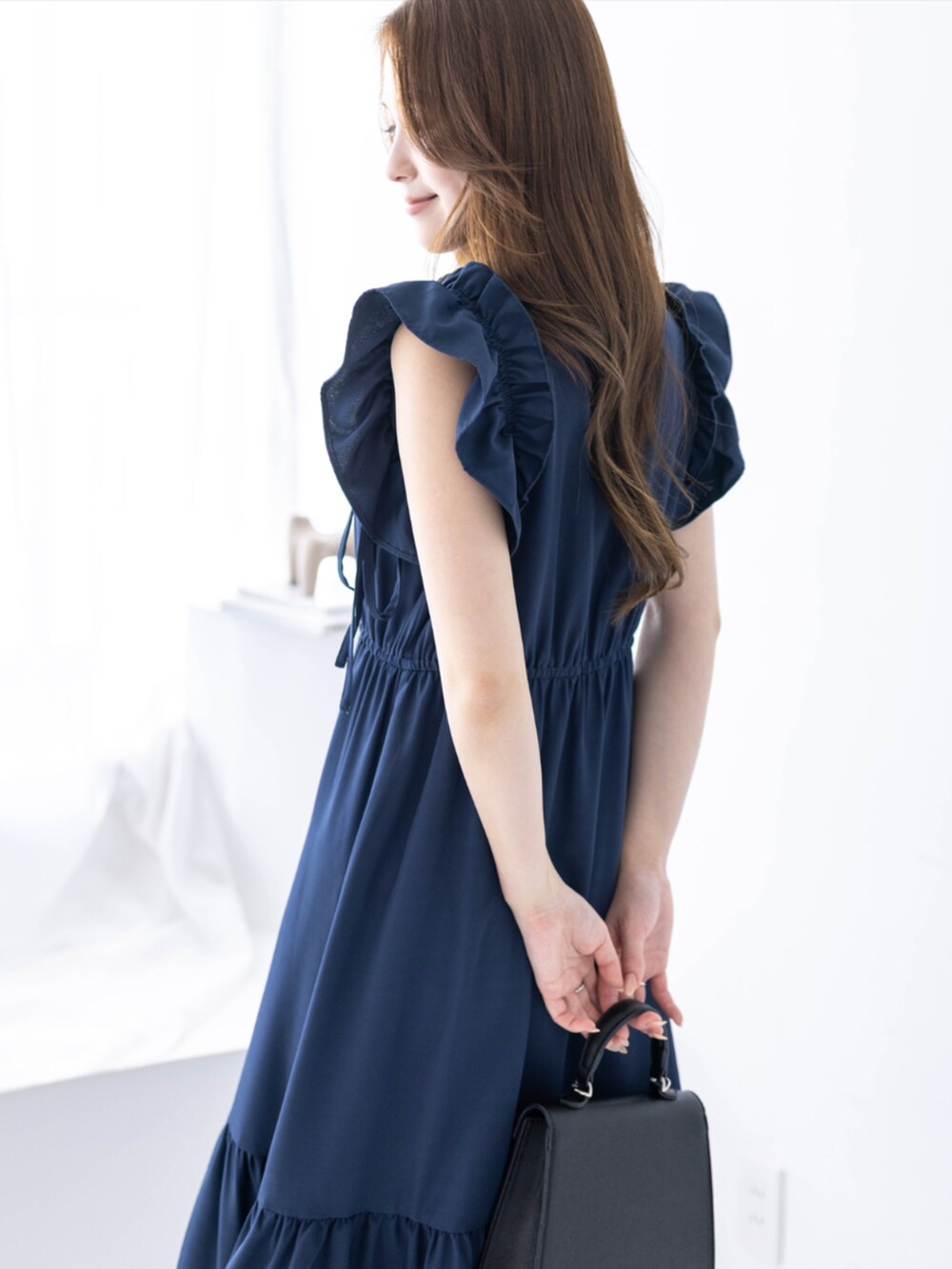 ブラック系のハンドバッグ、ブラック系のパンプス、ブルー系のワンピースを着用したレディースの春コーディネートの5枚目の写真