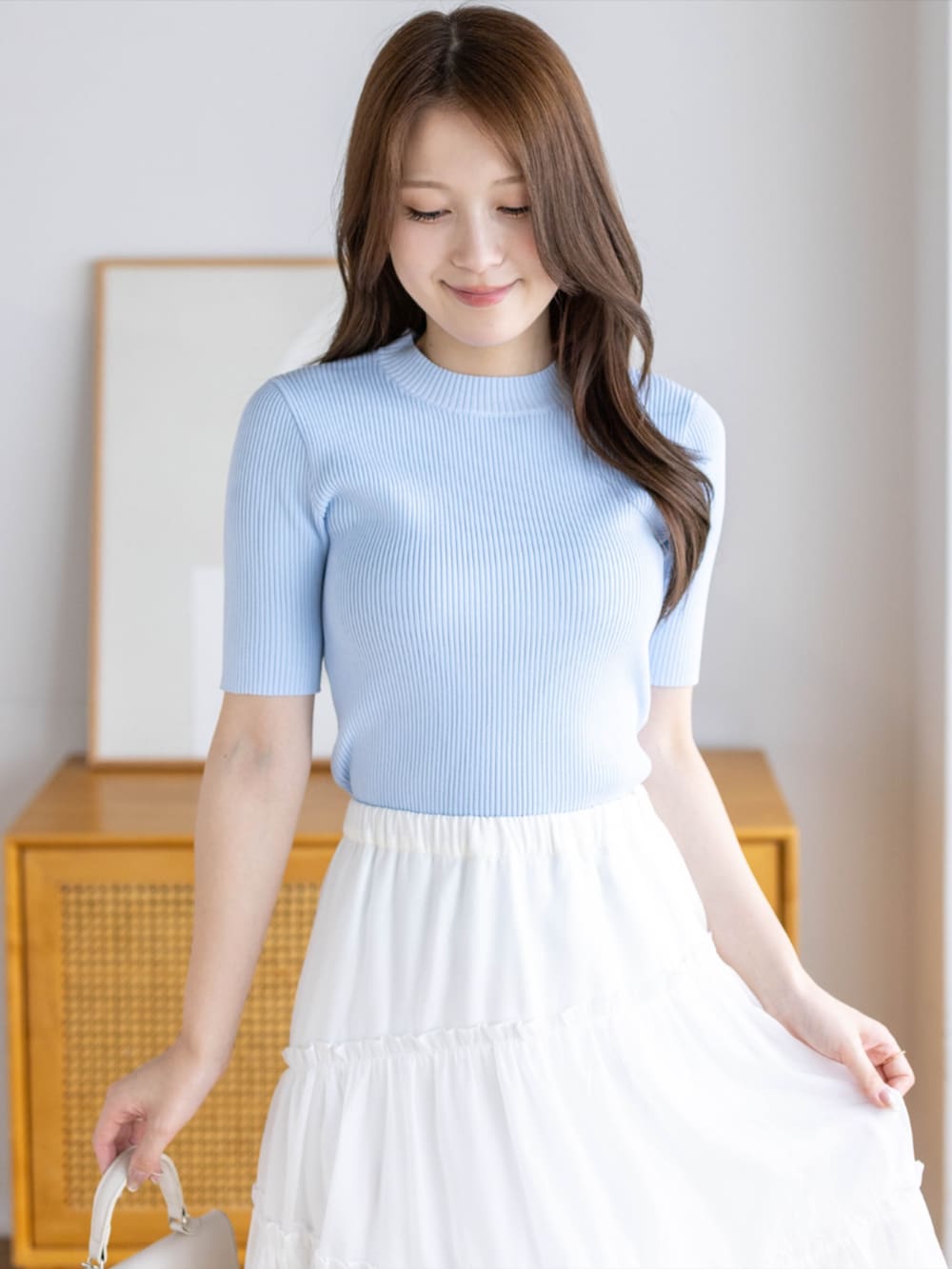 ブルー系のニット/セーター、ホワイト系のハンドバッグ、ホワイト系のパンプスを着用したレディースの夏コーディネートの3枚目の写真