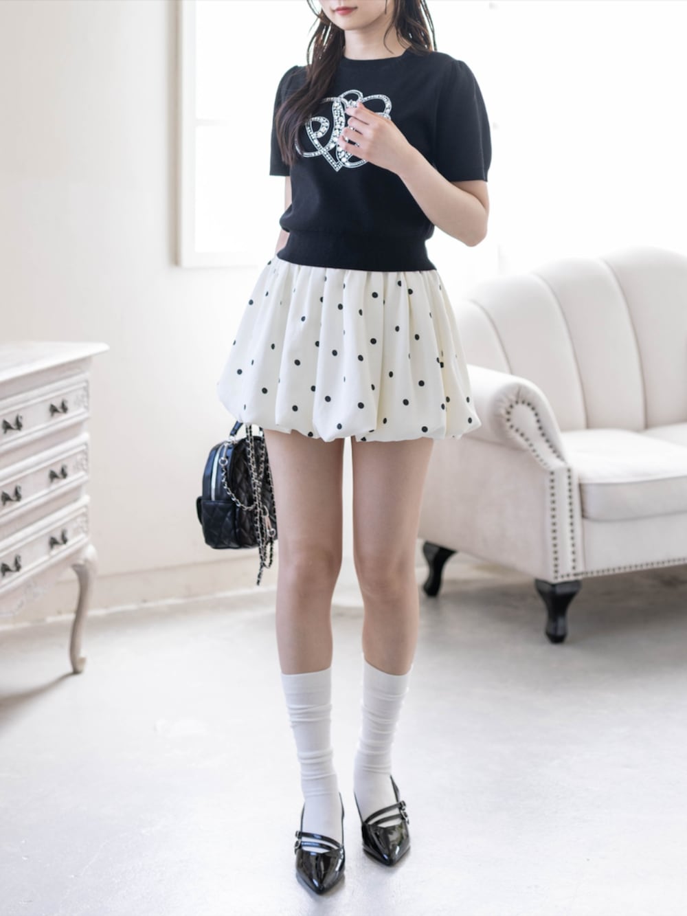 ブラック系のパンプス、ブラック系のニット/セーター、ホワイト系のスカートを着用したレディースの夏コーディネートの4枚目の写真
