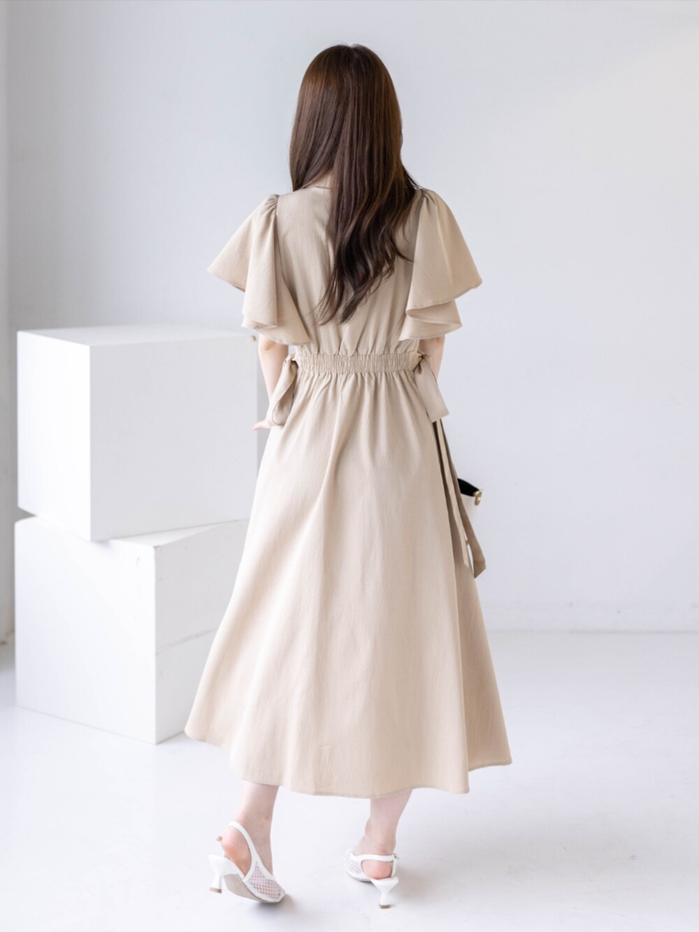 ホワイト系のパンプス、ベージュ系のワンピース、ベージュ系のハンドバッグを着用したレディースの夏コーディネートの2枚目の写真
