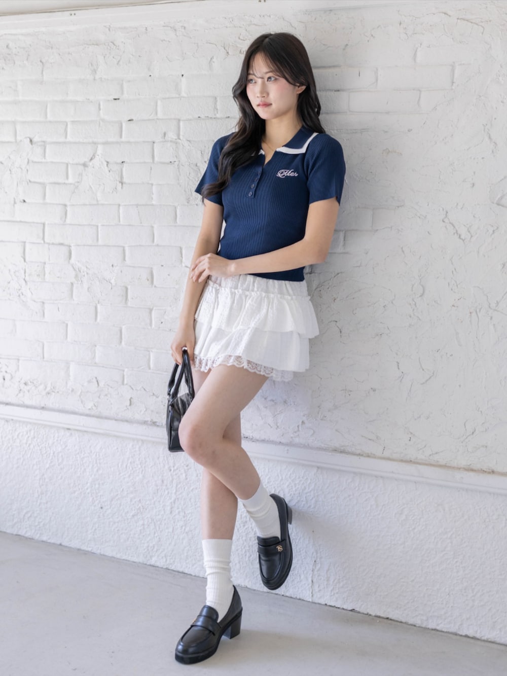 ブラック系のハンドバッグ、ブラック系のローファー、ホワイト系のスカートを着用したレディースの春コーディネートの2枚目の写真