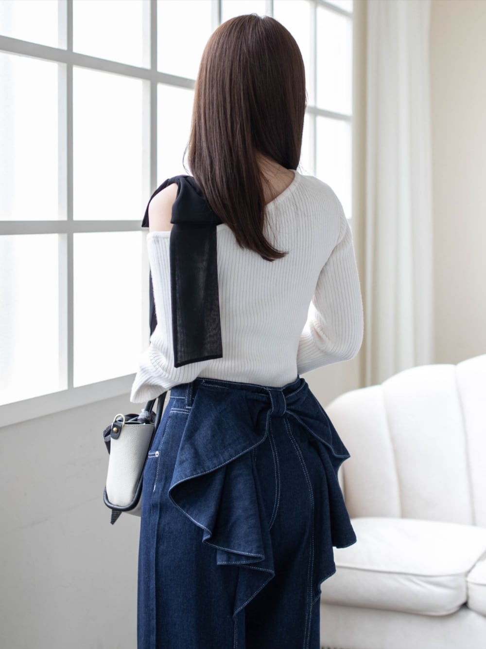 ブラック系のハンドバッグ、ブルー系のデニムパンツ、ブラック系のパンプスを着用したレディースの秋コーディネートの4枚目の写真