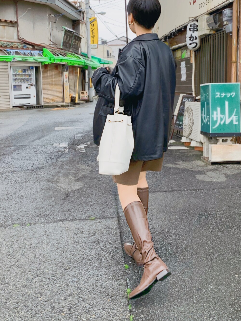 ブラック系のカバーオール、ホワイト系のニット/セーター、ブラウン系のブーツを着用したレディースの春コーディネートの2枚目の写真