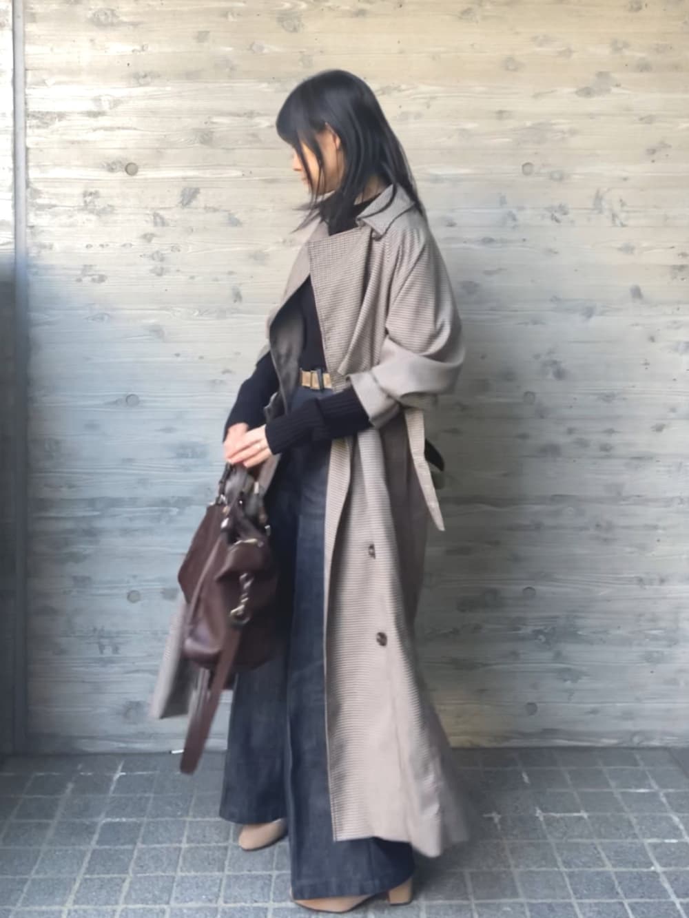 ブラック系のニット/セーター、ブラウン系のトレンチコート、ブルー系のデニムパンツを着用したレディースの春コーディネートの2枚目の写真