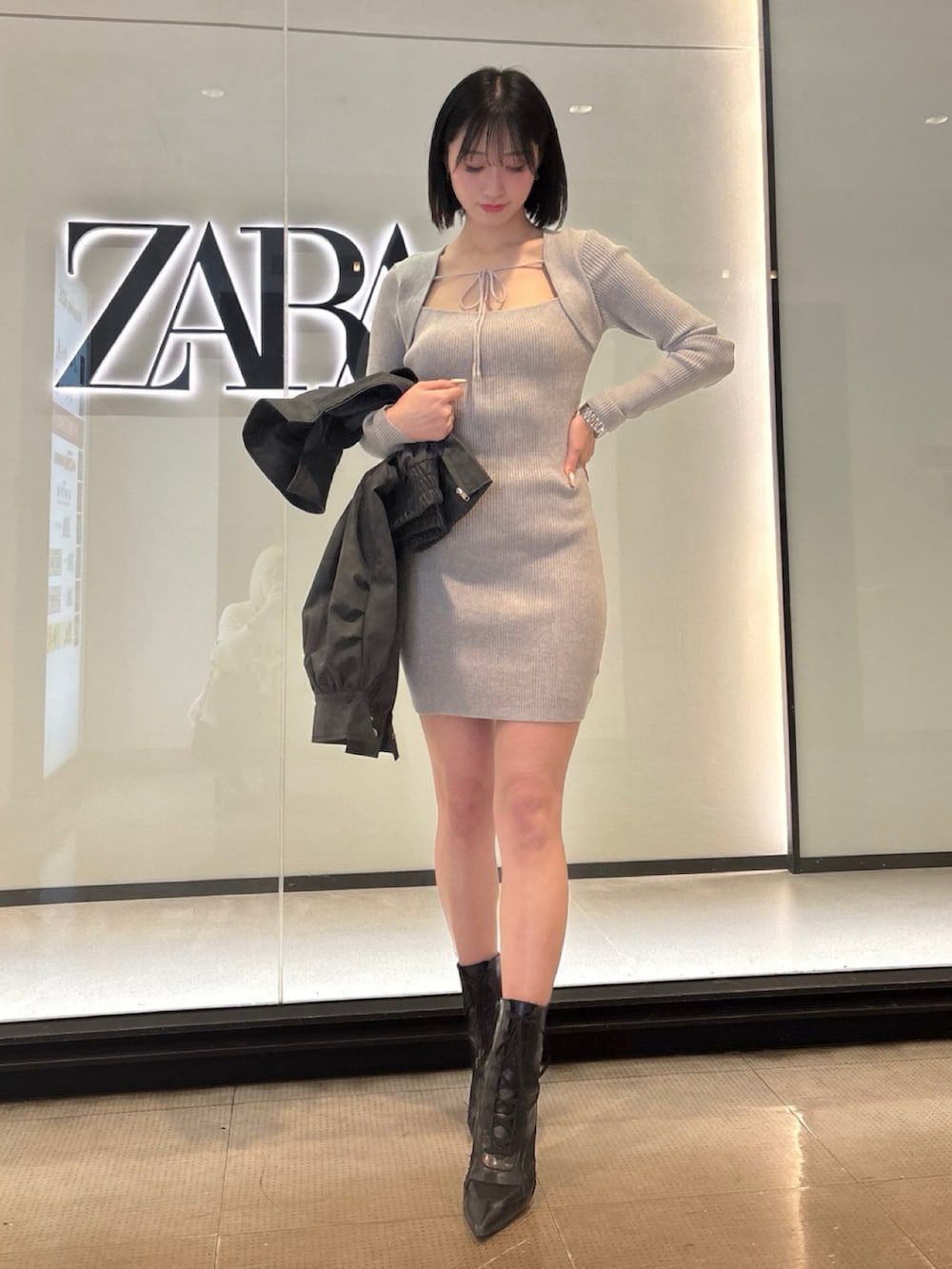 グレー系のワンピース、ブラック系のブルゾン、ブラック系のハンドバッグを着用したレディースの春コーディネートの2枚目の写真