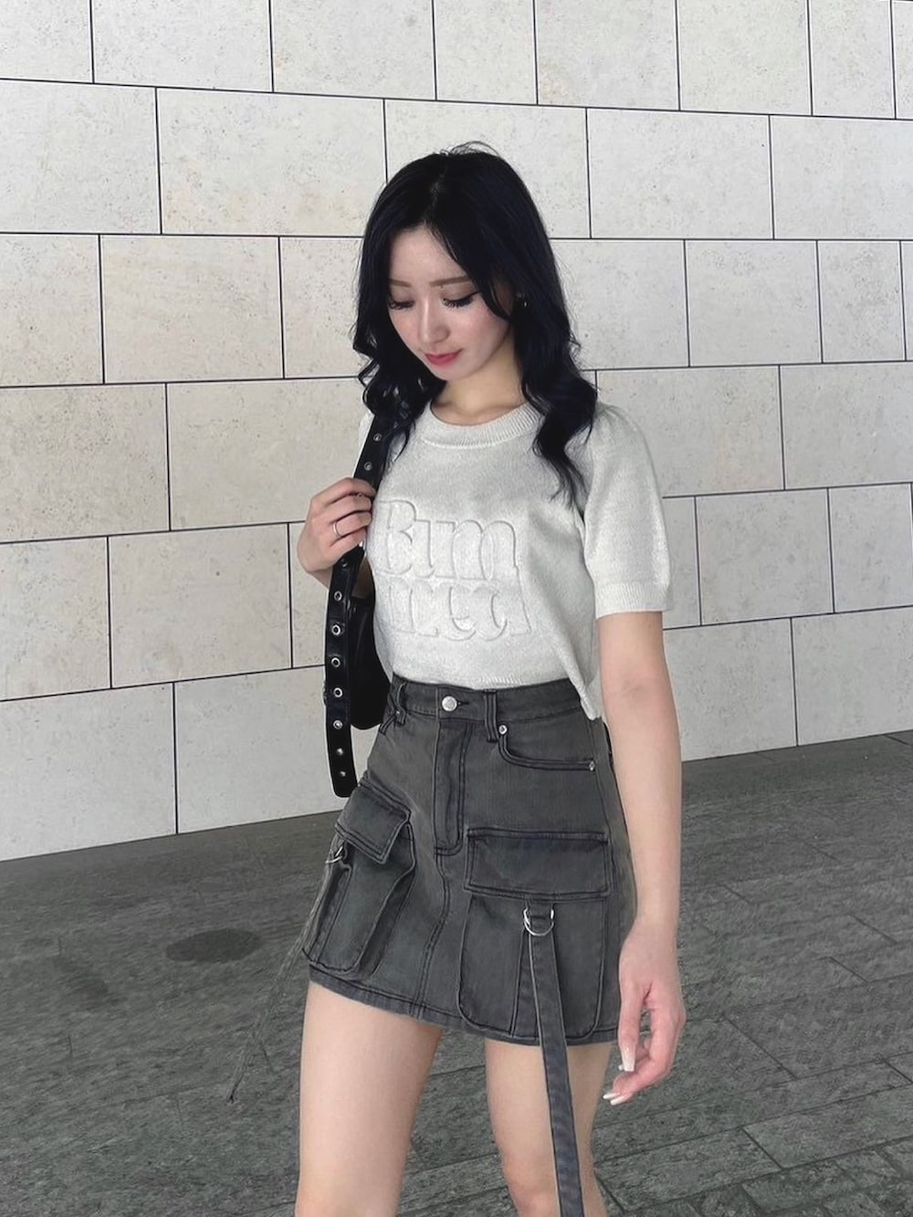 ブラック系のデニムスカート、ホワイト系のニット/セーター、ブラック系のサンダルを着用したレディースの夏コーディネートの2枚目の写真