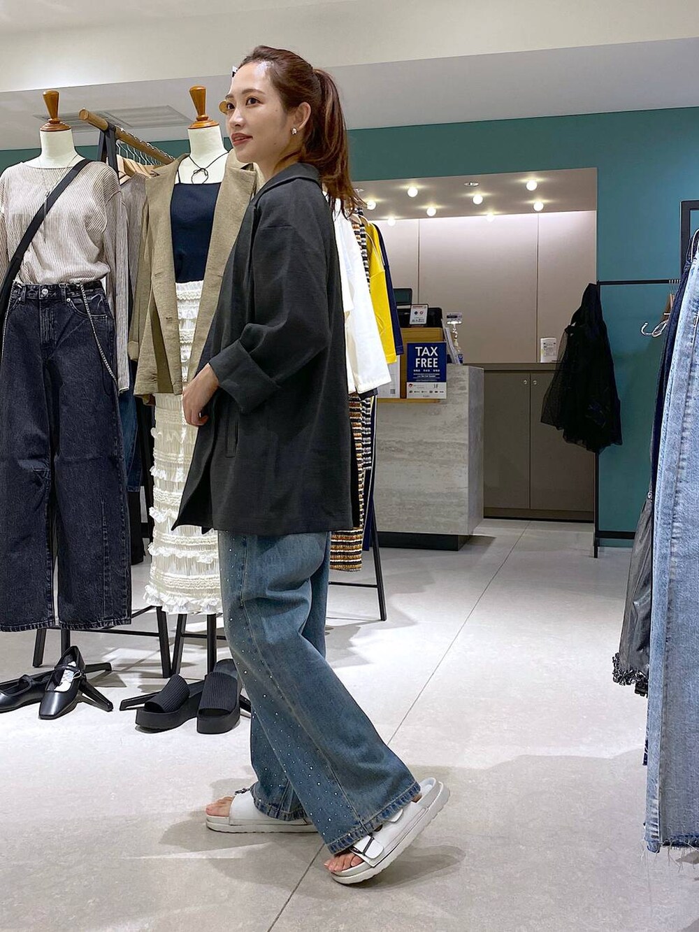 ブルー系のデニムパンツ、グレー系のテーラードジャケット、ホワイト系のサンダルを着用したレディースの秋コーディネートの4枚目の写真