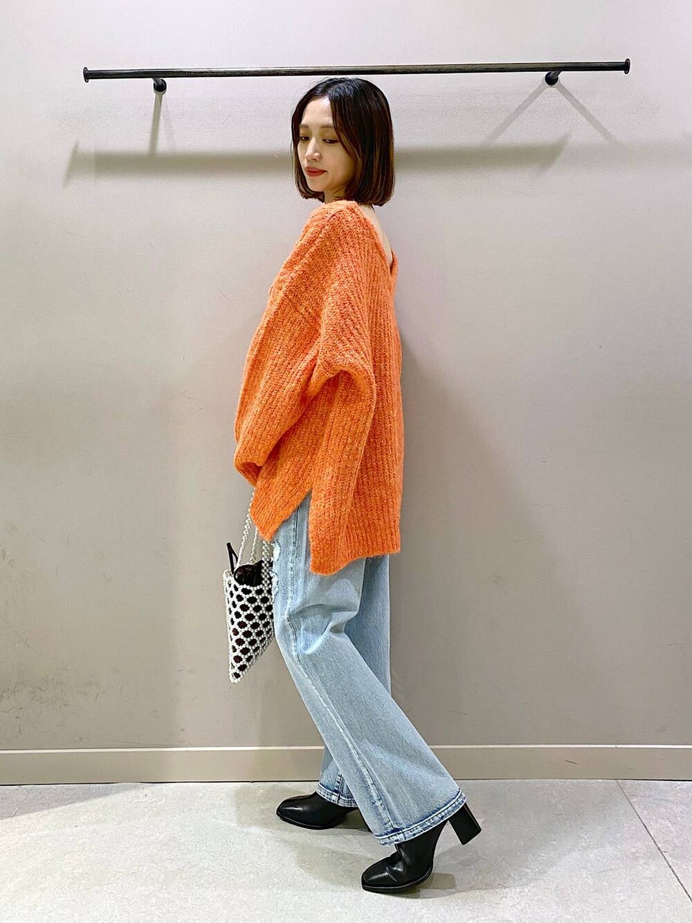 ブルー系のデニムパンツ、オレンジ系のニット/セーター、ブラック系のパンプスを着用したレディースの秋コーディネートの2枚目の写真