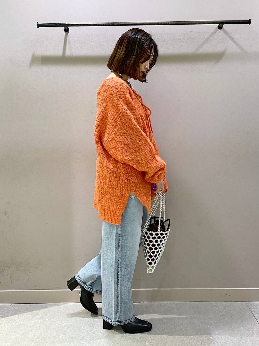 ブルー系のデニムパンツ、オレンジ系のニット/セーター、ブラック系のパンプスを着用したレディースの秋コーディネートの4枚目の写真