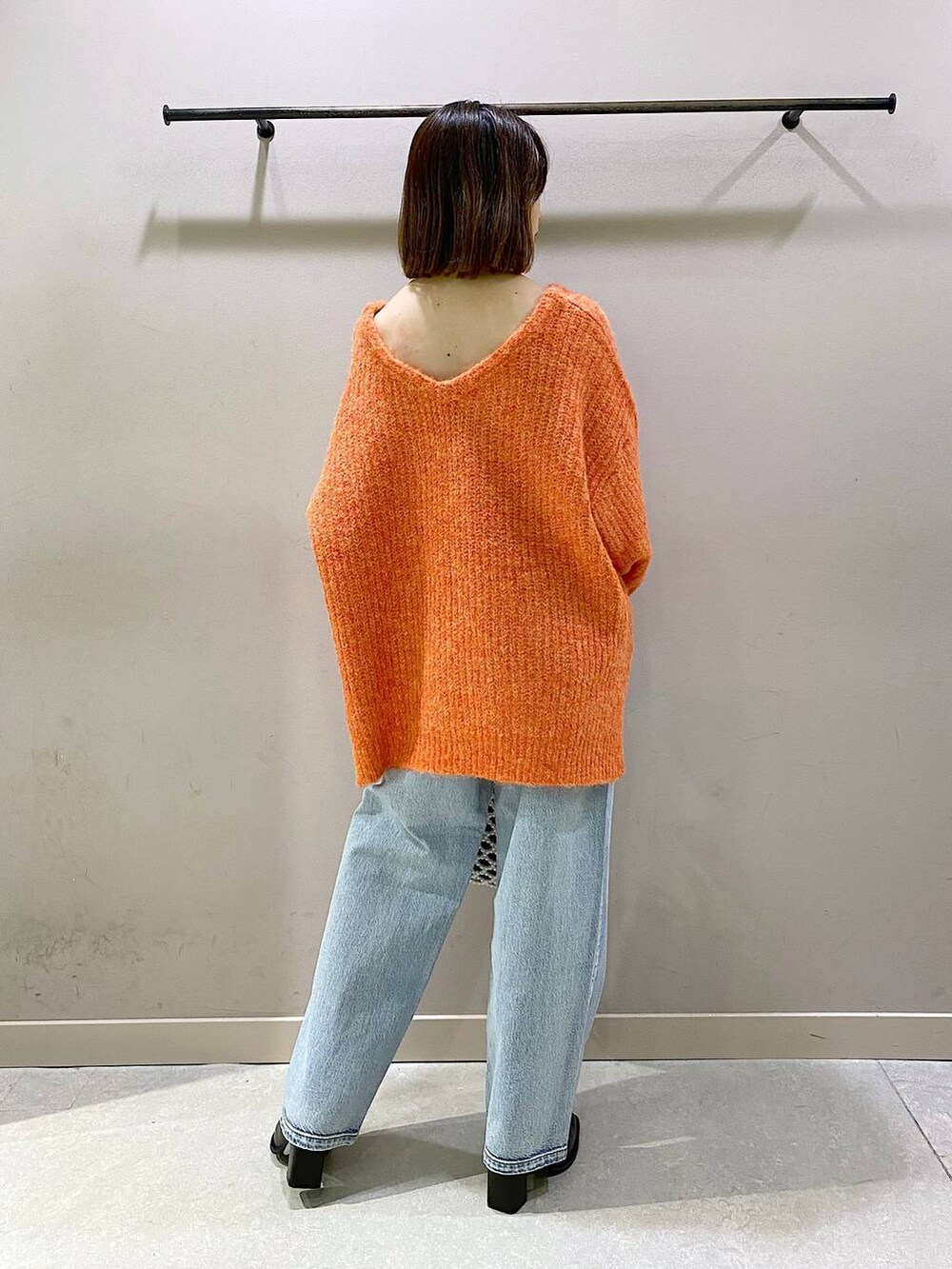 ブルー系のデニムパンツ、オレンジ系のニット/セーター、ブラック系のパンプスを着用したレディースの秋コーディネートの3枚目の写真