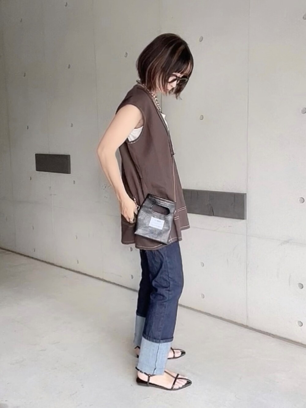 ブラウン系のベスト、ブルー系のデニムパンツ、ブラック系のサンダルを着用したレディースの夏コーディネートの3枚目の写真