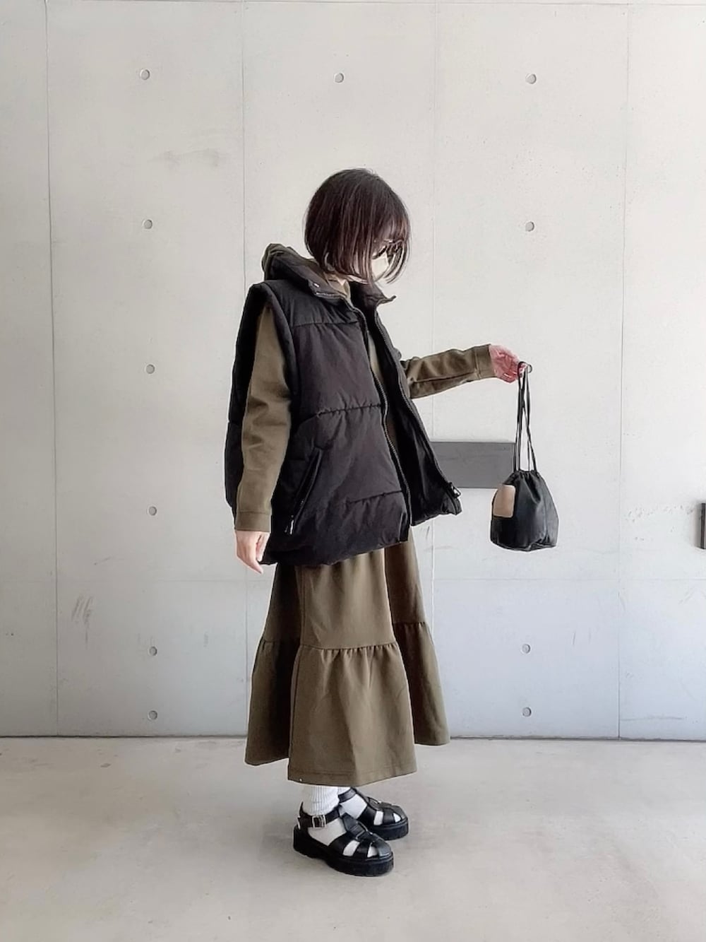 グリーン系のワンピース、ブラック系のダウンベスト、ブラック系のサンダルを着用したレディースの春コーディネートの4枚目の写真