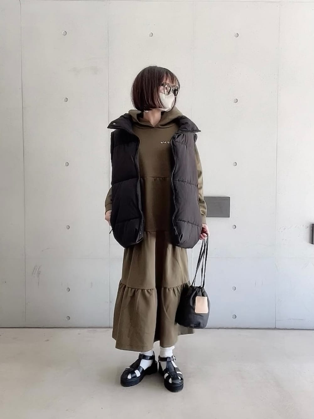 グリーン系のワンピース、ブラック系のダウンベスト、ブラック系のサンダルを着用したレディースの春コーディネートの3枚目の写真