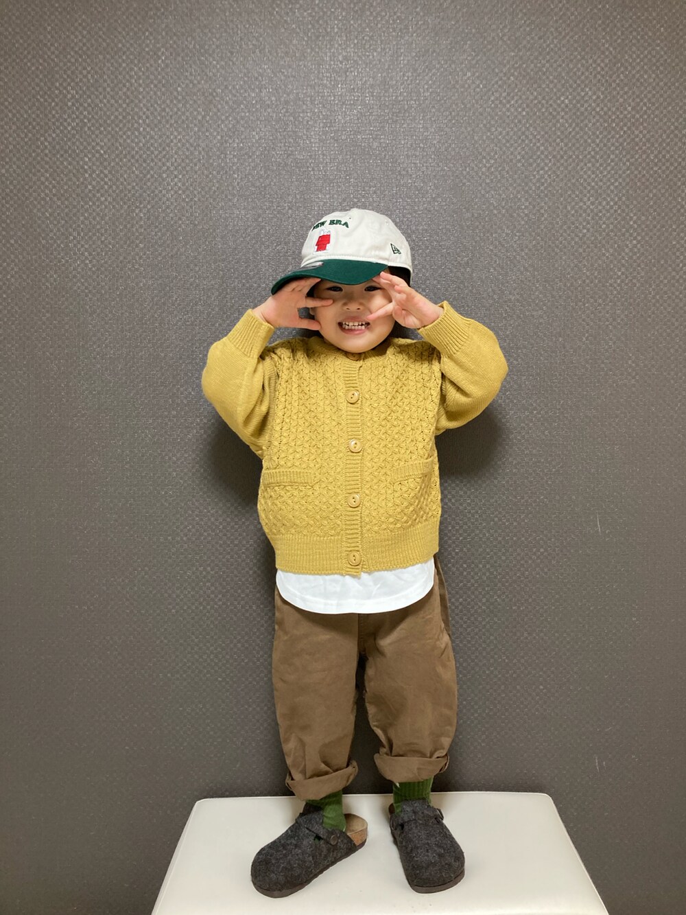 イエロー系のカーディガン/ボレロ、ブラウン系のチノパンツ、グレー系のサンダルを着用したキッズの冬コーディネートの4枚目の写真