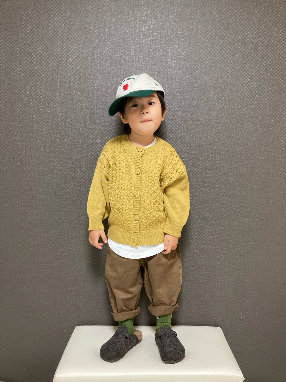 イエロー系のカーディガン/ボレロ、ブラウン系のチノパンツ、グレー系のサンダルを着用したキッズの冬コーディネートの2枚目の写真