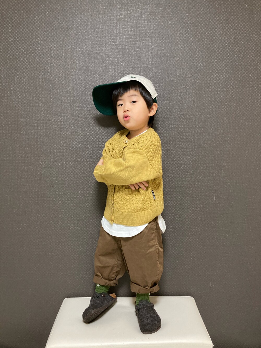 イエロー系のカーディガン/ボレロ、ブラウン系のチノパンツ、グレー系のサンダルを着用したキッズの冬コーディネートの3枚目の写真