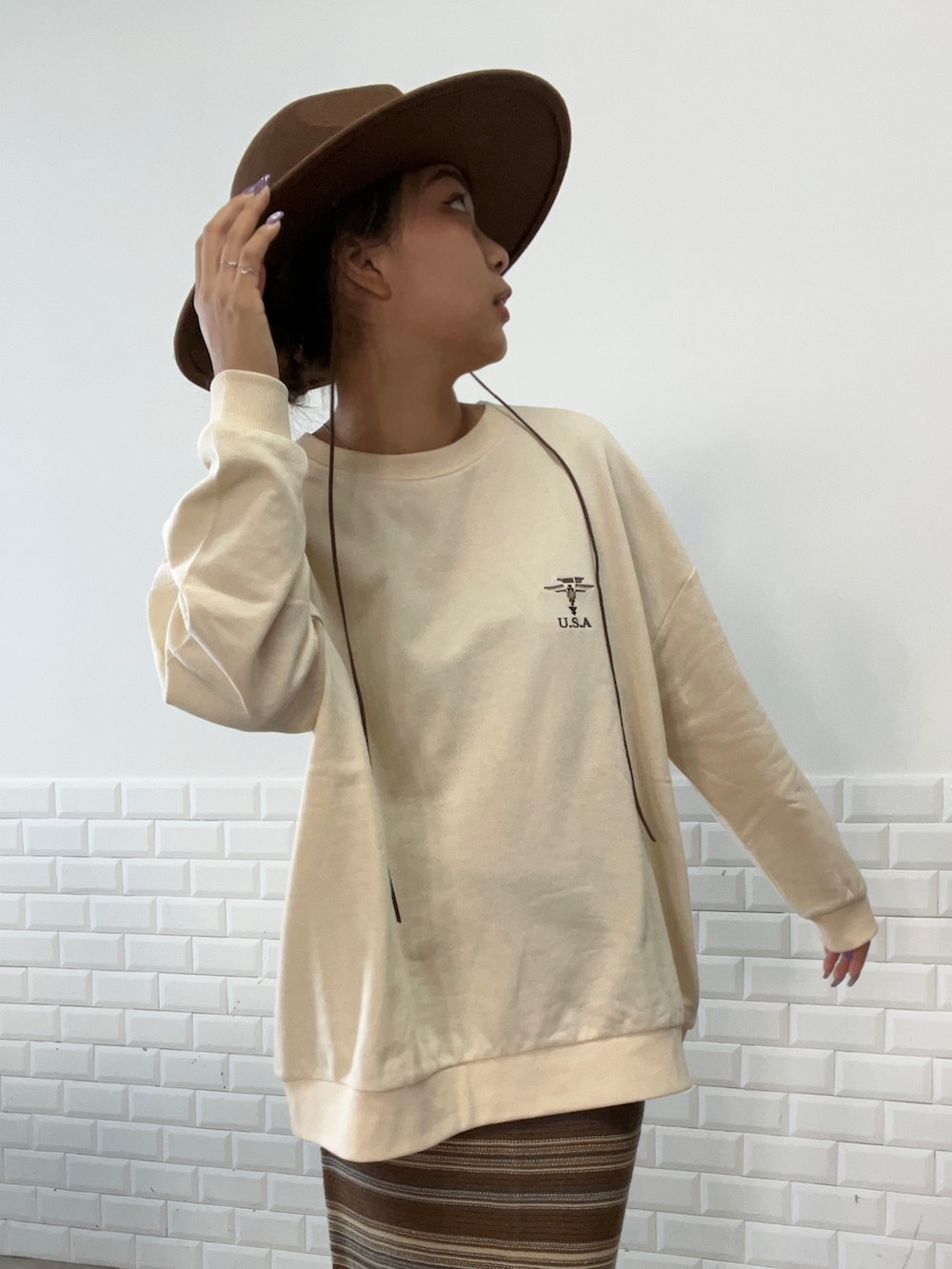 ブラウン系のスカート、ベージュ系のスウェット、ブラウン系のハットを着用したレディースの秋コーディネートの2枚目の写真