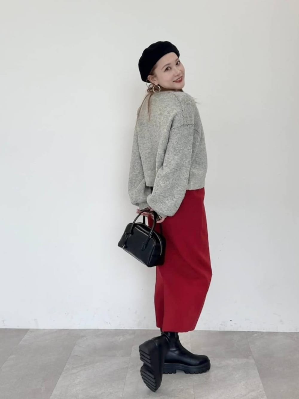 レッド系のスカート、ブラック系のブーツ、ブラック系のボストンバッグを着用したレディースの秋コーディネートの3枚目の写真