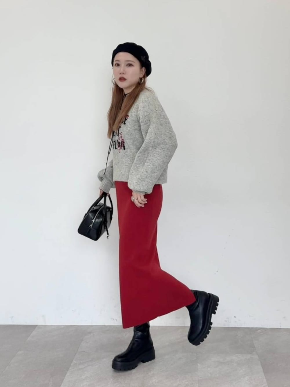 レッド系のスカート、ブラック系のブーツ、ブラック系のボストンバッグを着用したレディースの秋コーディネートの2枚目の写真