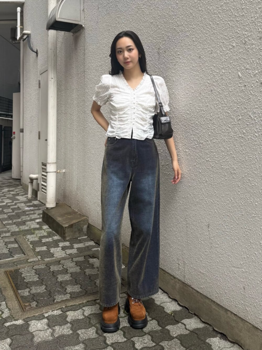 グリーン系のデニムパンツ、ブラウン系のブーツ、ブラック系のハンドバッグを着用したレディースの秋コーディネートの2枚目の写真