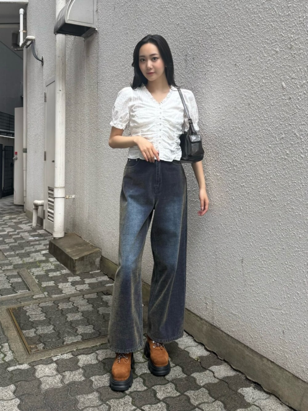 グリーン系のデニムパンツ、ブラウン系のブーツ、ブラック系のハンドバッグを着用したレディースの秋コーディネートの4枚目の写真