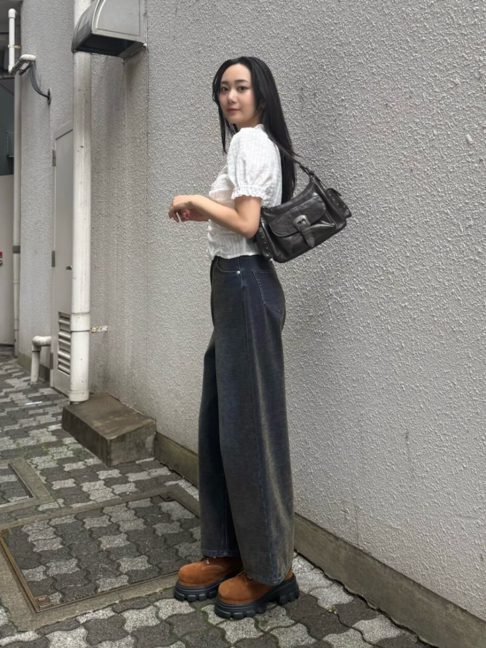 グリーン系のデニムパンツ、ブラウン系のブーツ、ブラック系のハンドバッグを着用したレディースの秋コーディネートの3枚目の写真