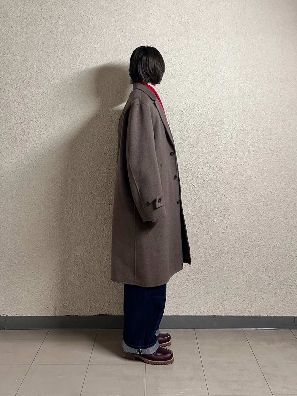 ブルー系のデニムパンツ、ホワイト系のニット/セーター、ブラウン系のチェスターコートを着用したメンズの春コーディネートの2枚目の写真