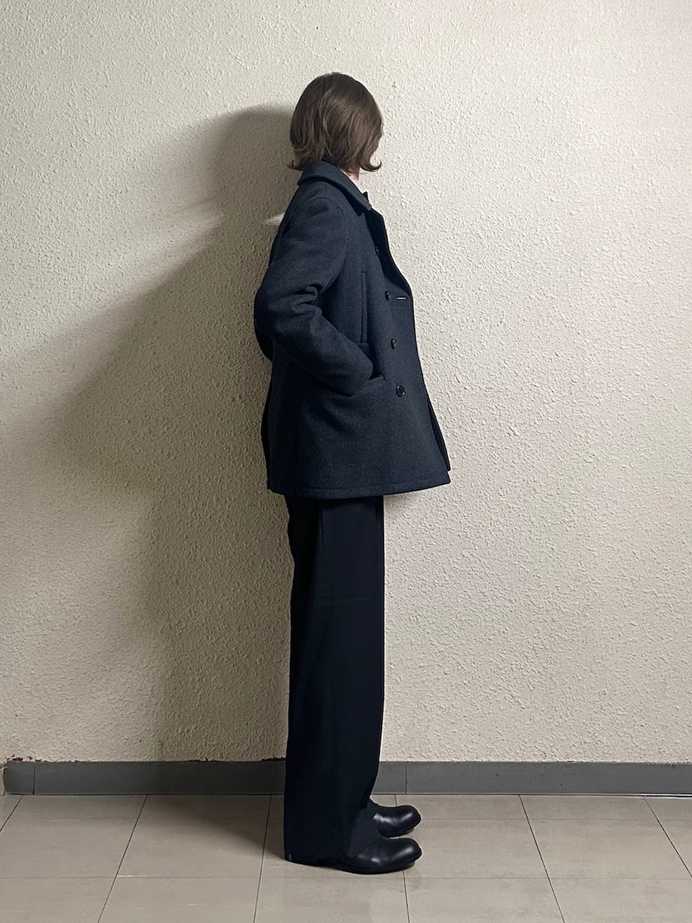 ブラック系のピーコート、グレー系のスラックス、ブラック系のライダースジャケットを着用したメンズの春コーディネートの2枚目の写真