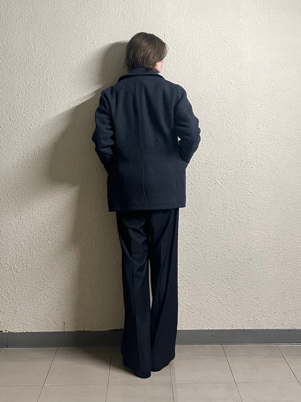 ブラック系のピーコート、グレー系のスラックス、ブラック系のライダースジャケットを着用したメンズの春コーディネートの3枚目の写真