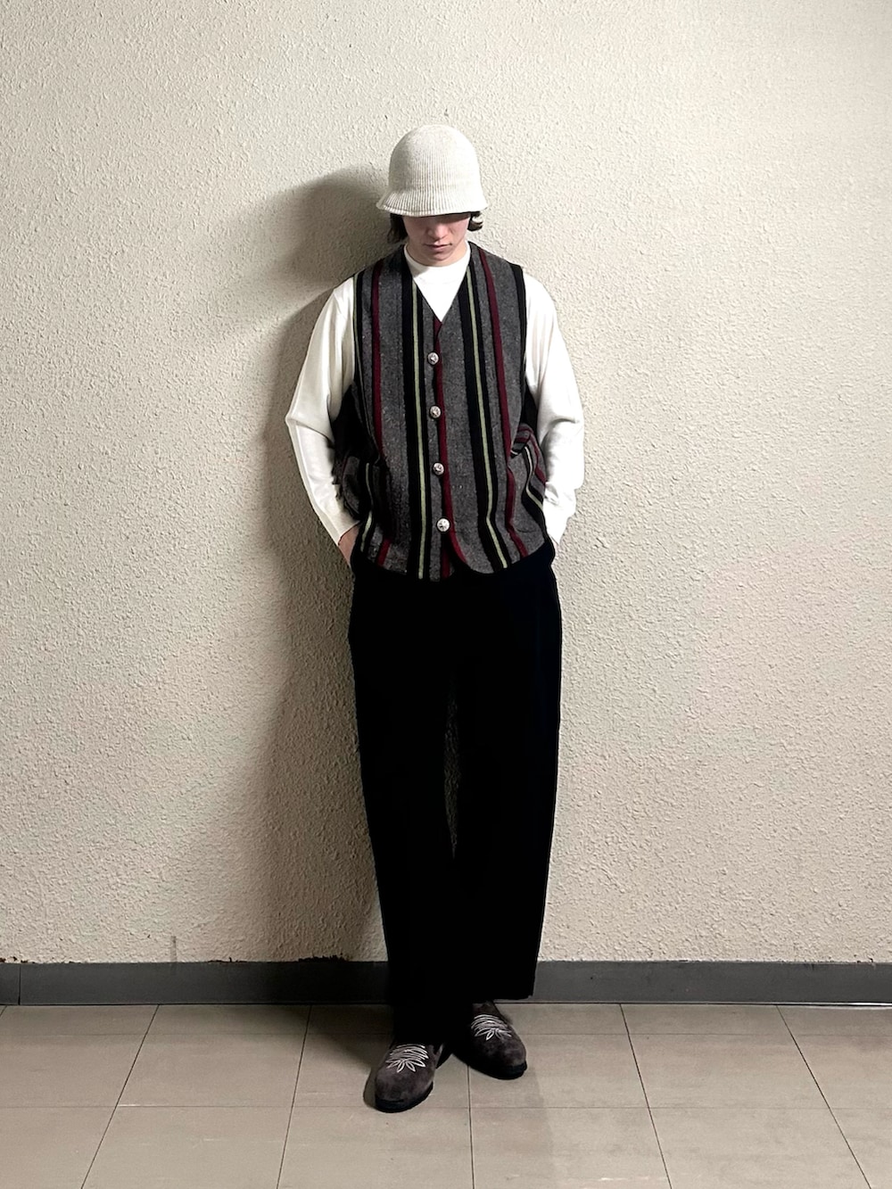 レッド系のベスト、ブラック系のパンツ、ブラウン系のシューズを着用したメンズの春コーディネートの4枚目の写真