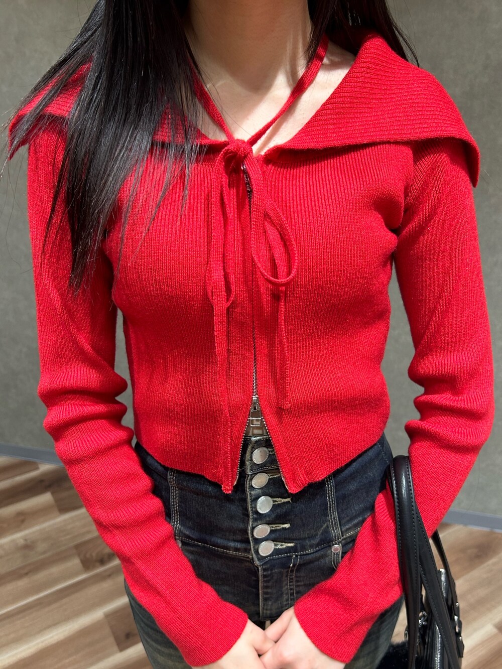 レッド系のニット/セーター、ブルー系のデニムパンツ、ブラック系のショルダーバッグを着用したレディースの秋コーディネートの5枚目の写真