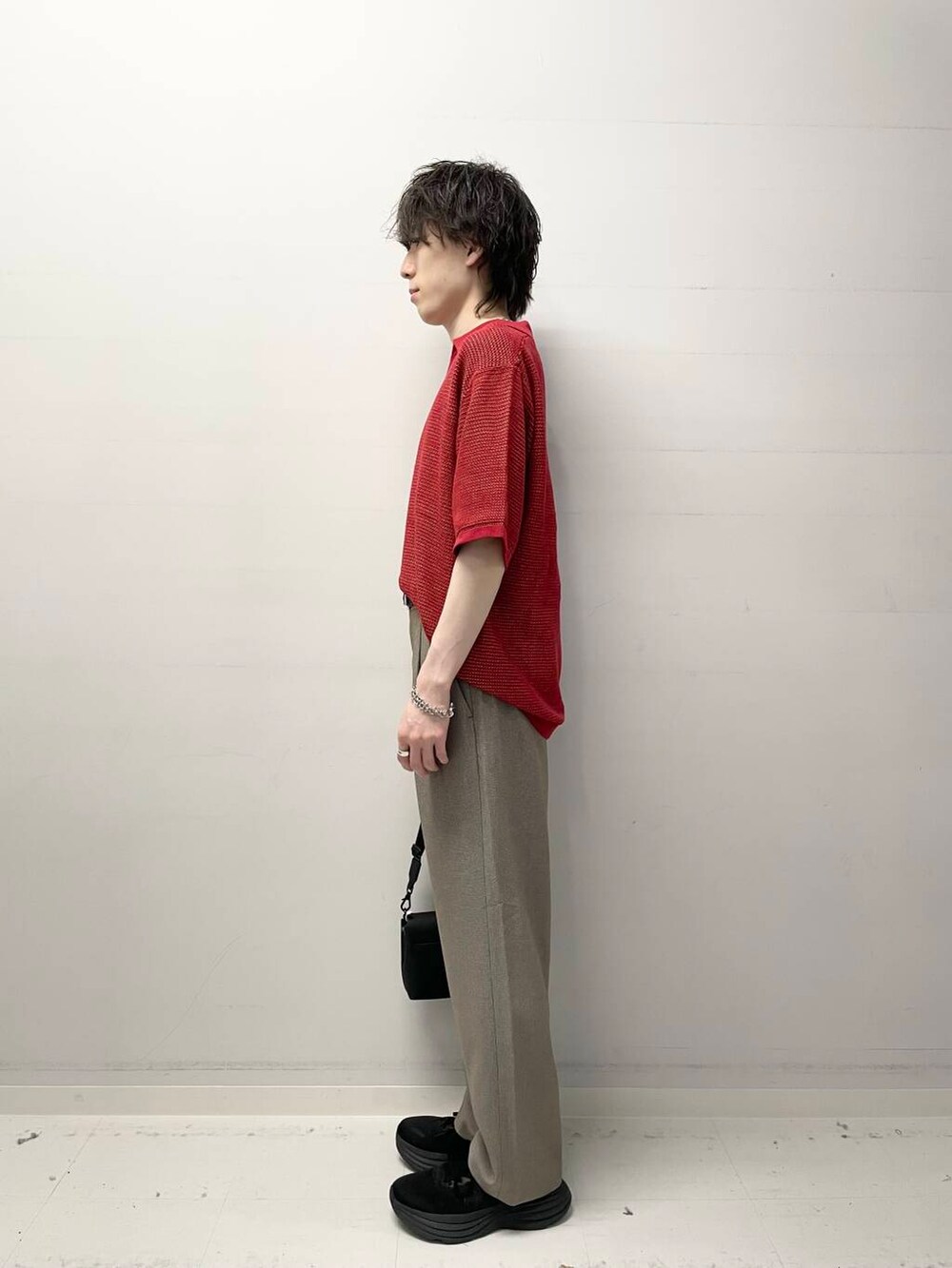 レッド系のニット/セーター、ブラック系のショルダーバッグ、ブラウン系のその他パンツを着用したメンズの春コーディネートの2枚目の写真