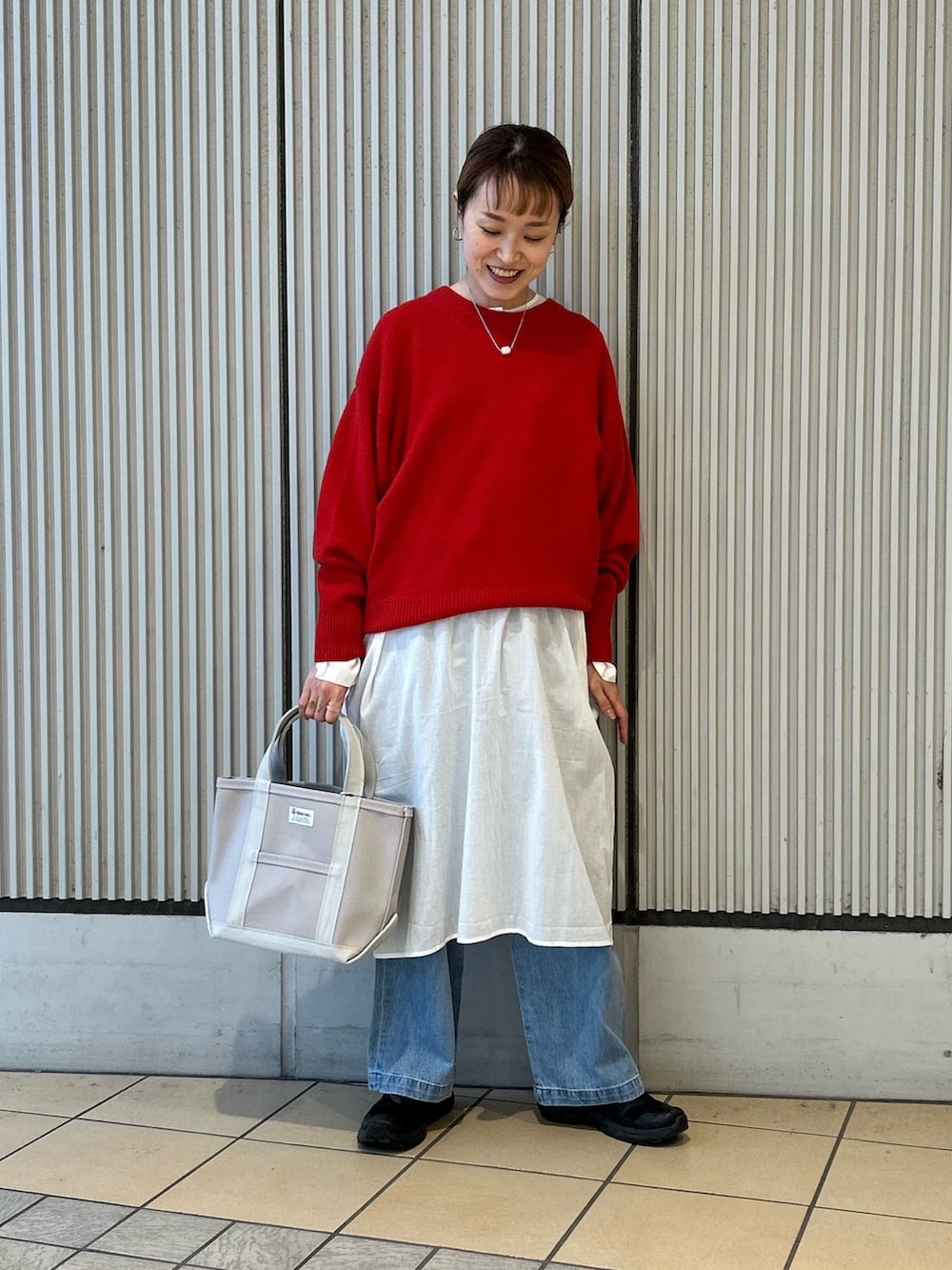 レッド系のニット/セーター、ブルー系のデニムパンツ、グレー系のトートバッグを着用したレディースの冬コーディネートの3枚目の写真