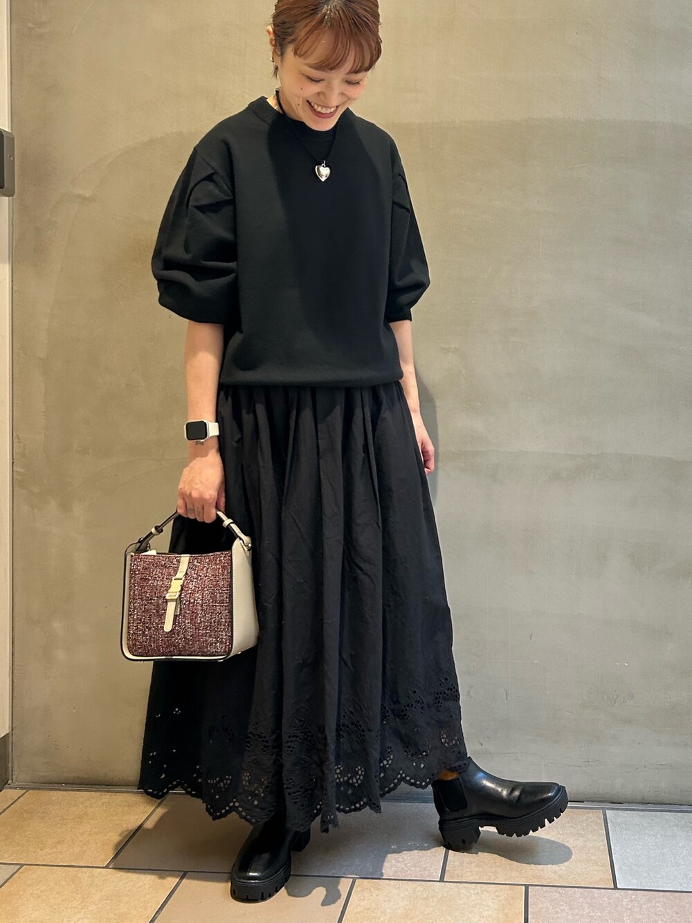 ブラック系のニット/セーター、ブラック系のスカート、レッド系のショルダーバッグを着用したレディースの秋コーディネートの3枚目の写真