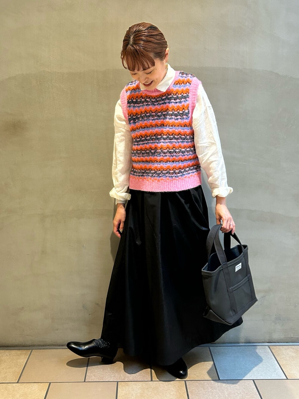 ピンク系のベスト、ブラック系のスカート、グレー系のトートバッグを着用したレディースの秋コーディネートの5枚目の写真