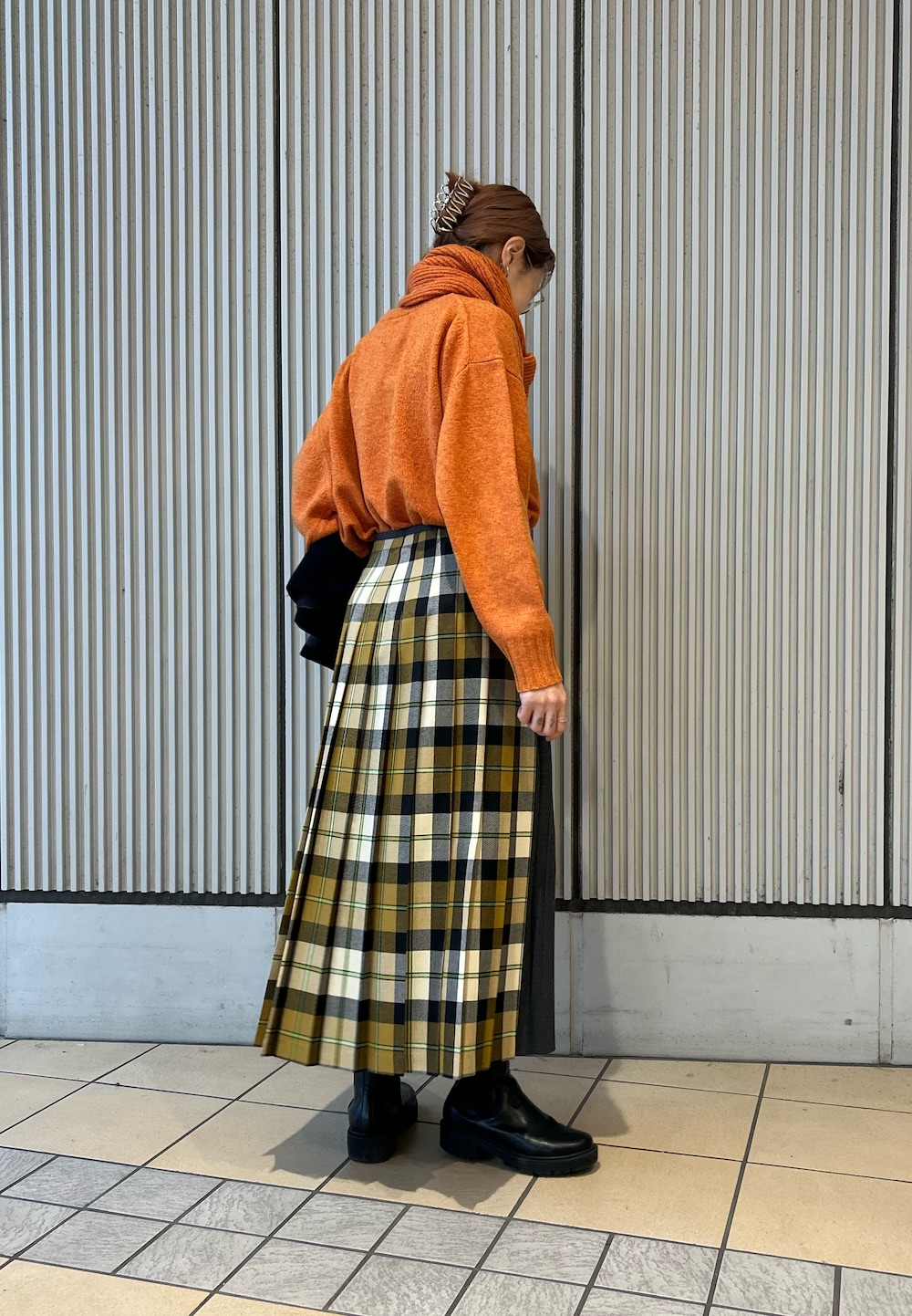 オレンジ系のニット/セーター、ベージュ系のスカート、ブラック系のハンドバッグを着用したレディースの冬コーディネートの2枚目の写真