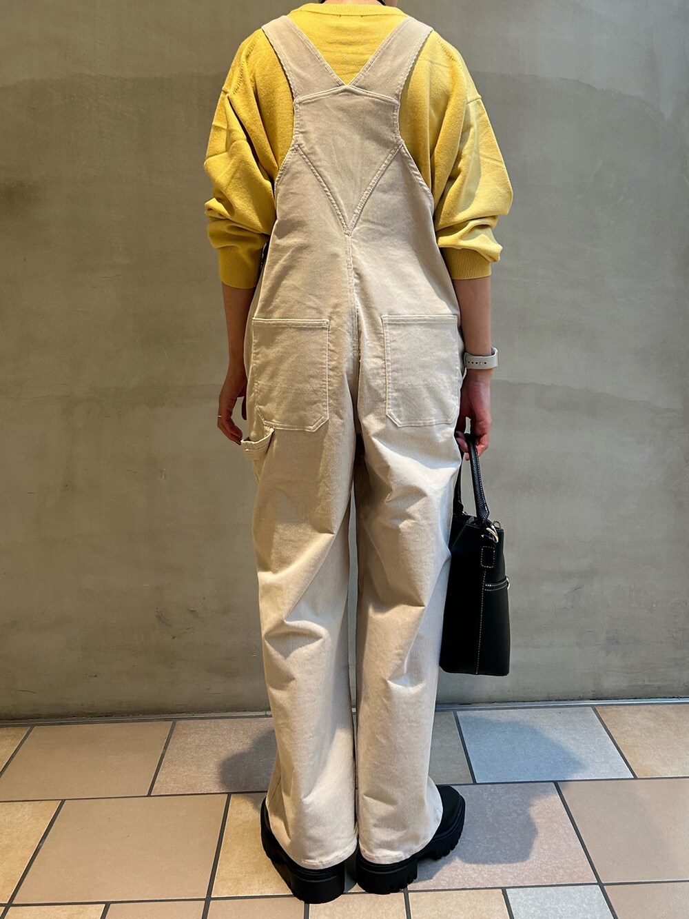 ホワイト系のサロペット/オーバーオール、イエロー系のニット/セーター、ブラック系のハンドバッグを着用したレディースの秋コーディネートの3枚目の写真