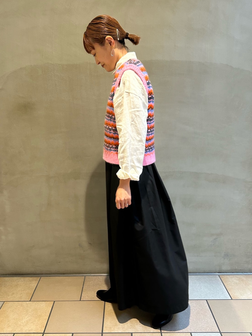 ピンク系のベスト、ブラック系のスカート、グレー系のトートバッグを着用したレディースの秋コーディネートの3枚目の写真