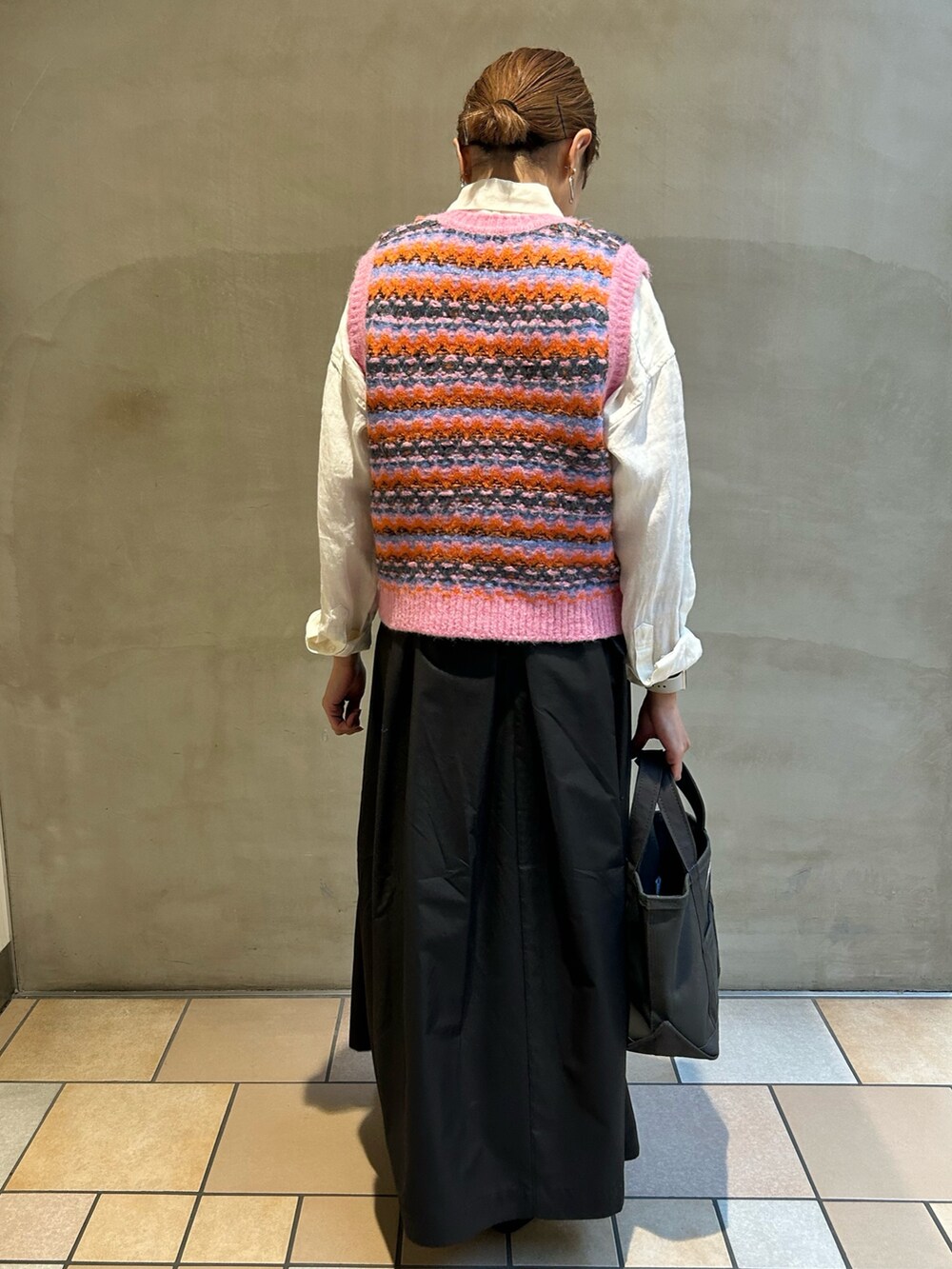 ピンク系のベスト、ブラック系のスカート、グレー系のトートバッグを着用したレディースの秋コーディネートの4枚目の写真