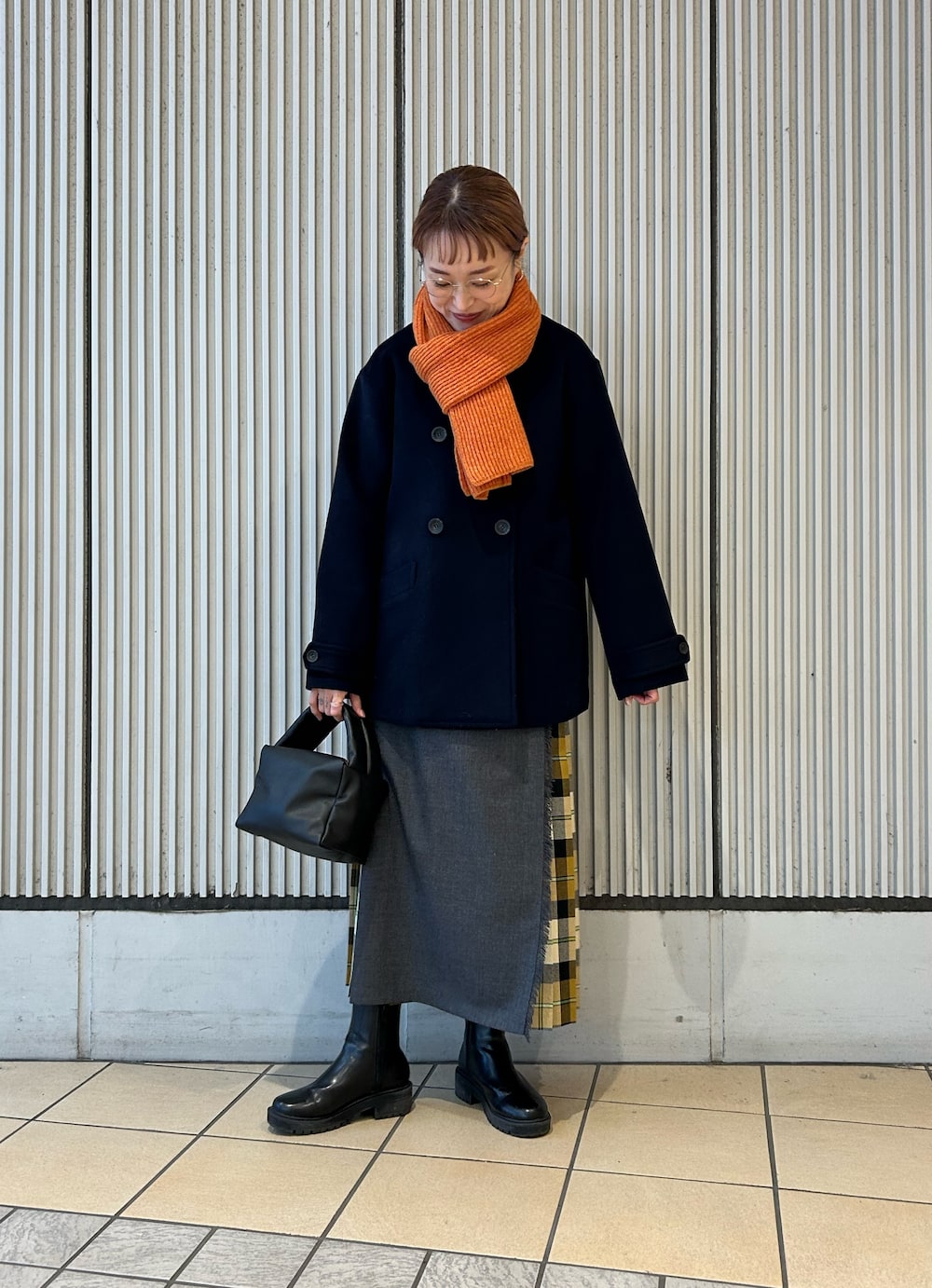 オレンジ系のニット/セーター、ベージュ系のスカート、ブラック系のハンドバッグを着用したレディースの冬コーディネートの4枚目の写真