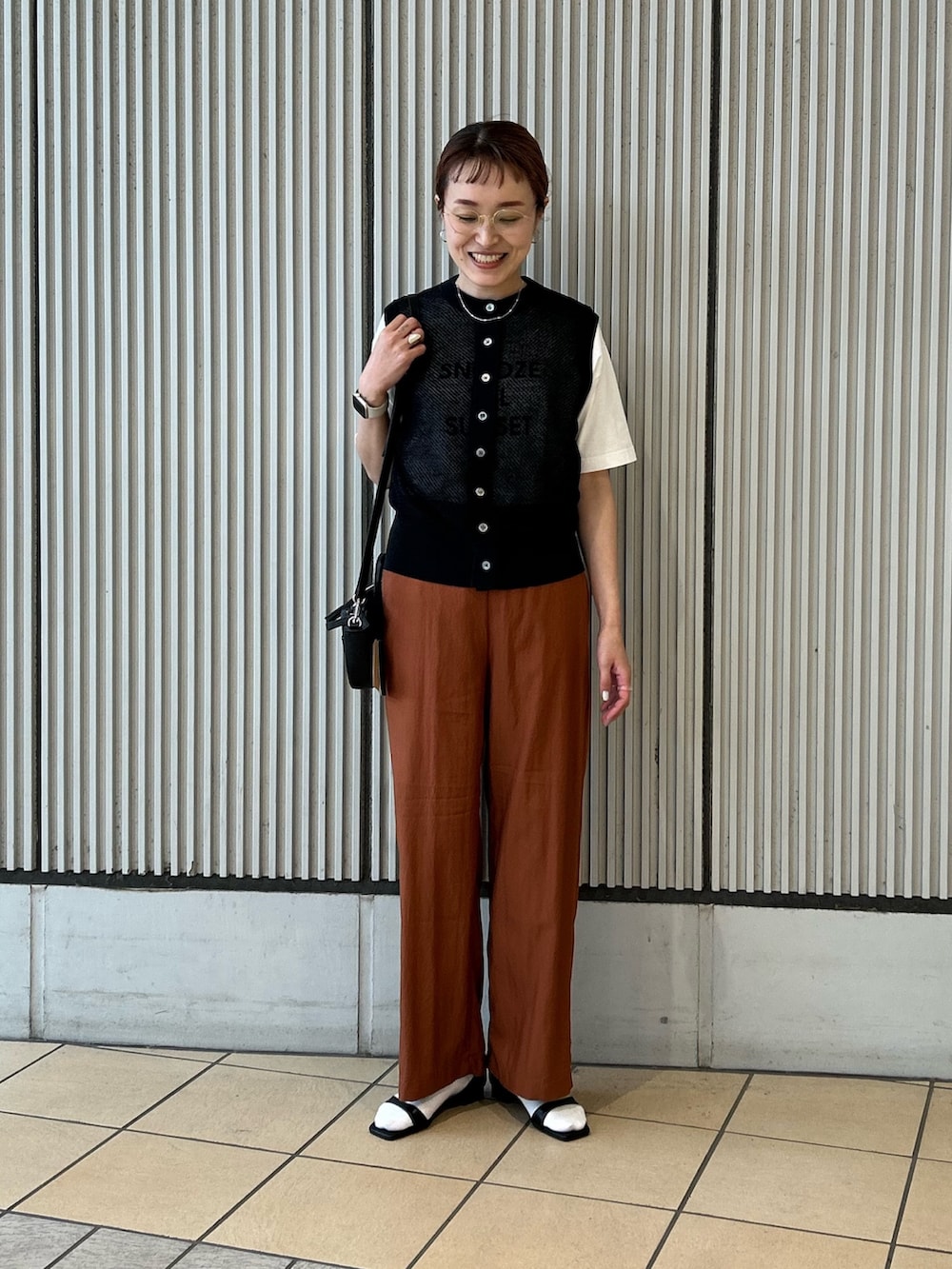 オレンジ系のその他パンツ、ブラック系のベスト、ブラック系のショルダーバッグを着用したレディースの春コーディネートの2枚目の写真
