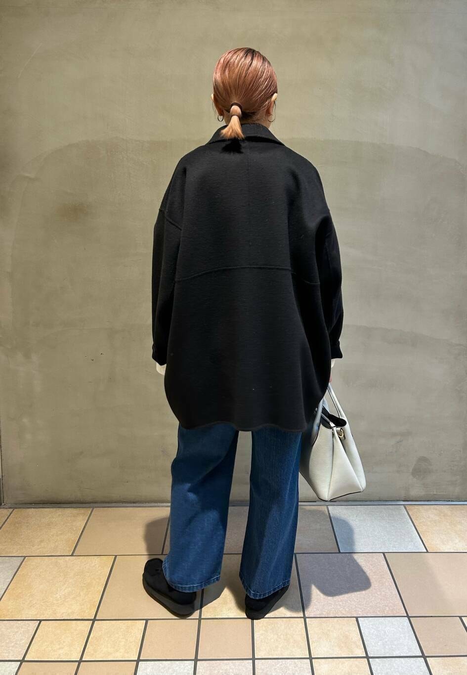 ブラック系のブーツ、ホワイト系のショルダーバッグ、ブルー系のデニムパンツを着用したレディースの冬コーディネートの5枚目の写真