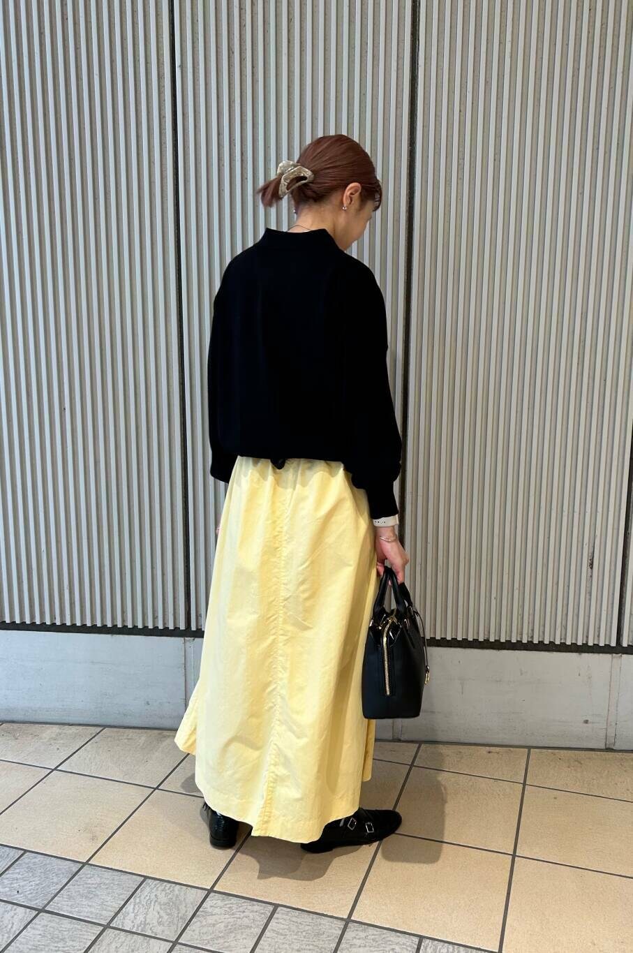ブラック系のハンドバッグ、イエロー系のスカート、ブラック系のニット/セーターを着用したレディースの春コーディネートの2枚目の写真