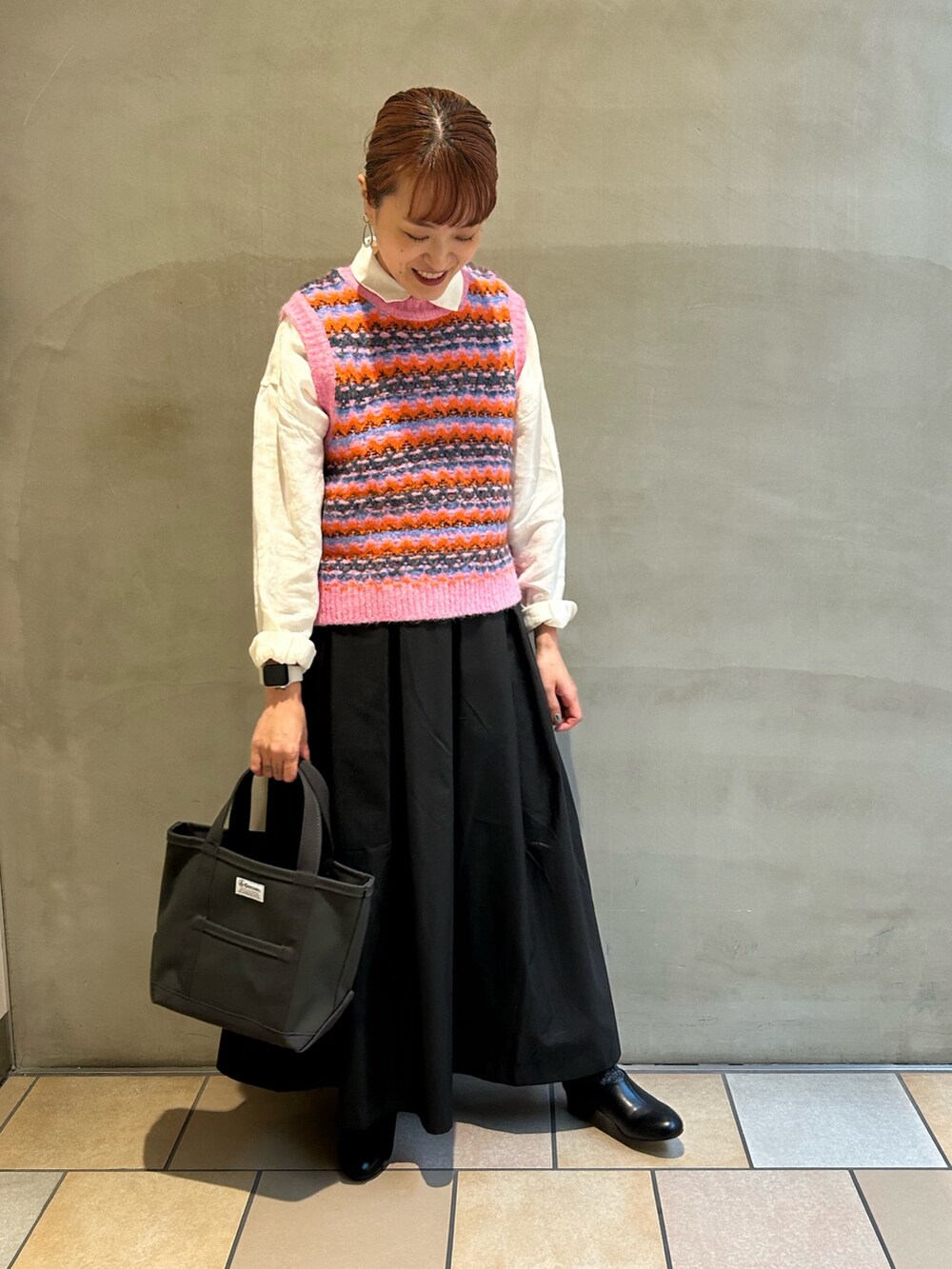 ピンク系のベスト、ブラック系のスカート、グレー系のトートバッグを着用したレディースの秋コーディネートの2枚目の写真