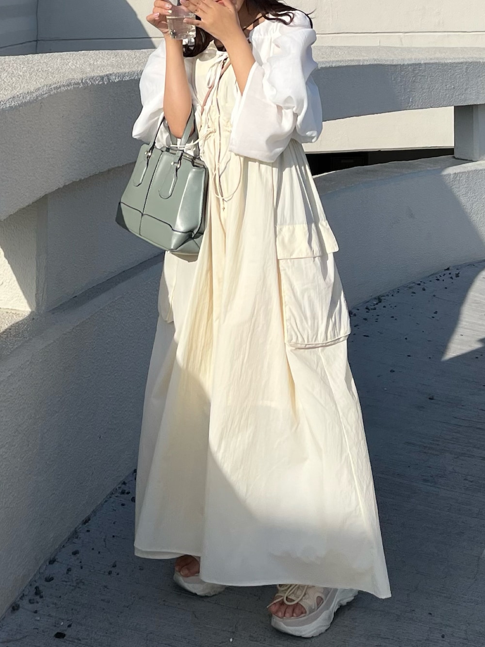 グリーン系のバッグ、ベージュ系のサンダル、ベージュ系のワンピースを着用したレディースの春コーディネートの4枚目の写真