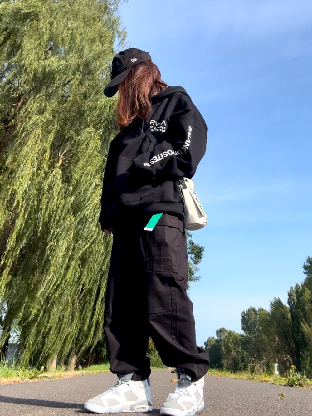 ブラック系のパーカー、ホワイト系のスニーカー、ホワイト系のショルダーバッグを着用したレディースの秋コーディネートの2枚目の写真