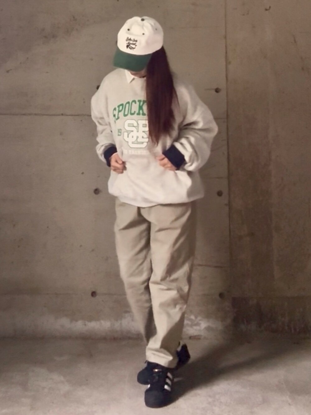 グレー系のスウェット、ブラック系のスニーカー、グリーン系のキャップを着用したレディースの秋コーディネートの2枚目の写真